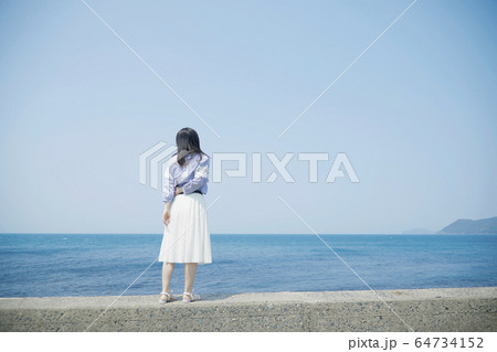 女性 堤防 後ろ姿 海の写真素材