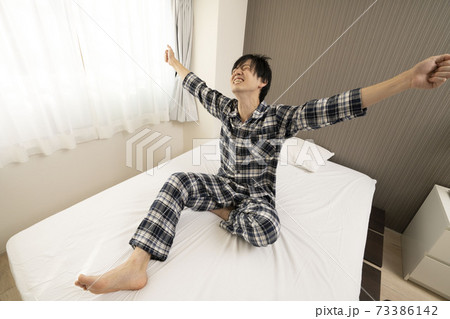 爽やかな朝を迎えた男性/パジャマ姿の独身男性/ベッドルーム/背伸びする男性	
