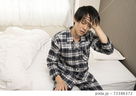 寝起きに発熱がわかり、体調が悪くなって会社に行けないパジャマ姿の男性	