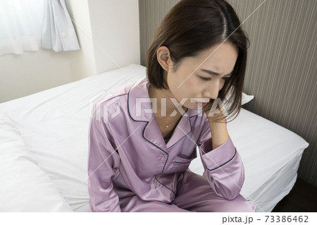 病気で寝込んでいる女性/体調の悪い女性/ベットに寝ている美しい女性/ベッドに座っている美人