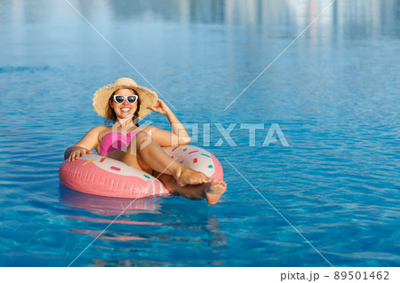 Happy woman in swimsuit floating on rubber ring in swimming pool